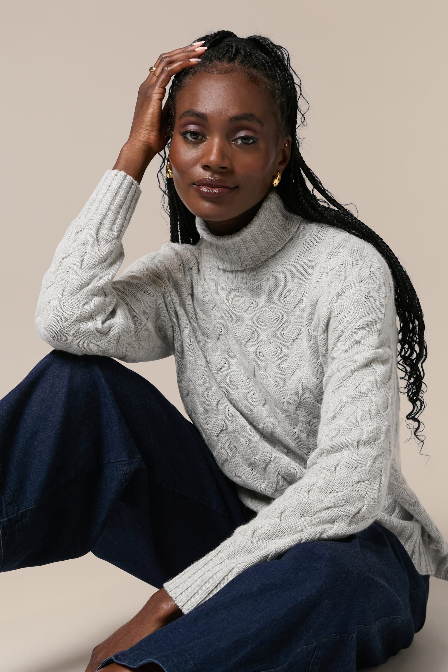 A black woman wearing a high-quality Cable Knit Jumper turtleneck sweater and blue pants.