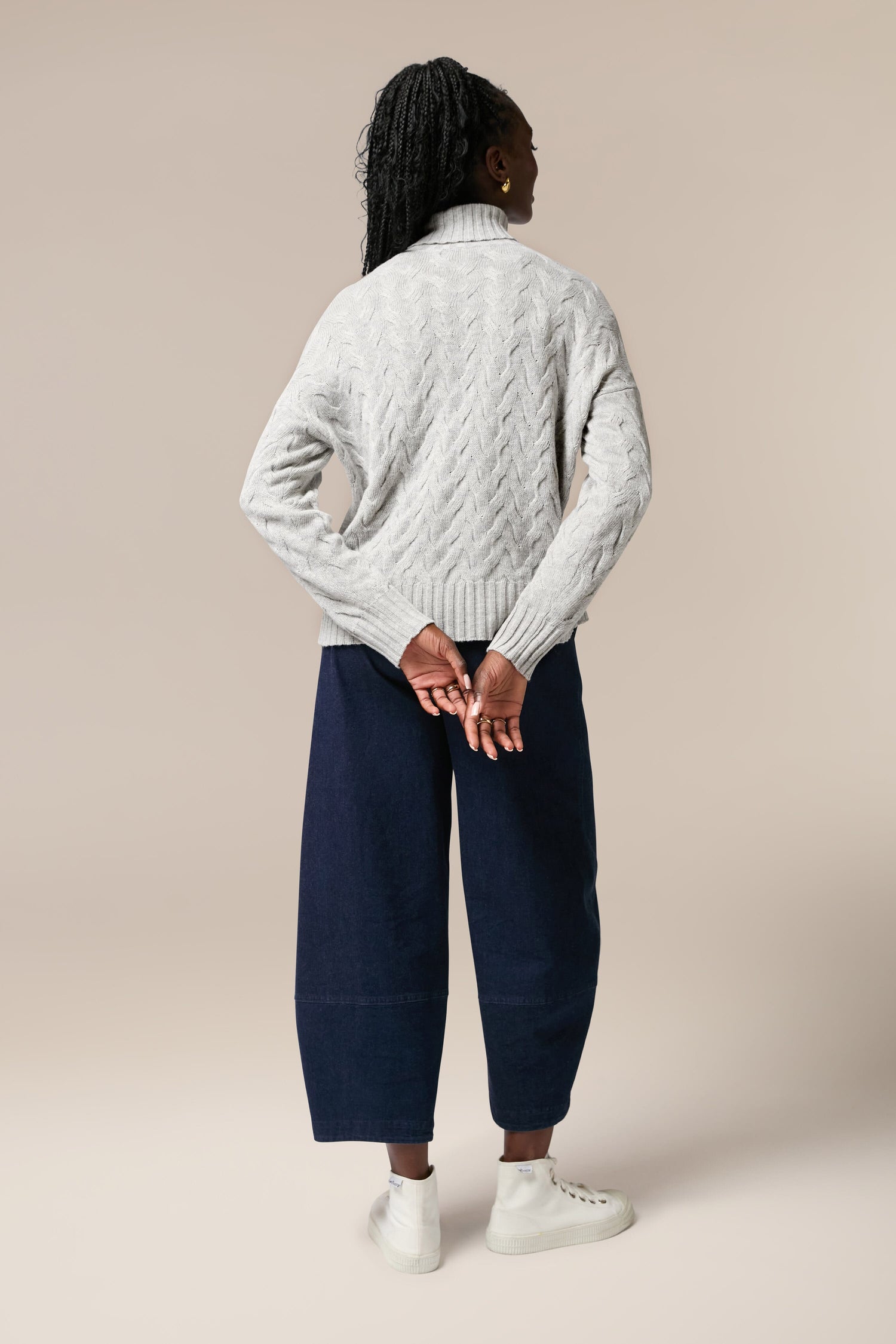 The back view of a woman wearing a high-quality Cable Knit Jumper and navy wide leg pants.