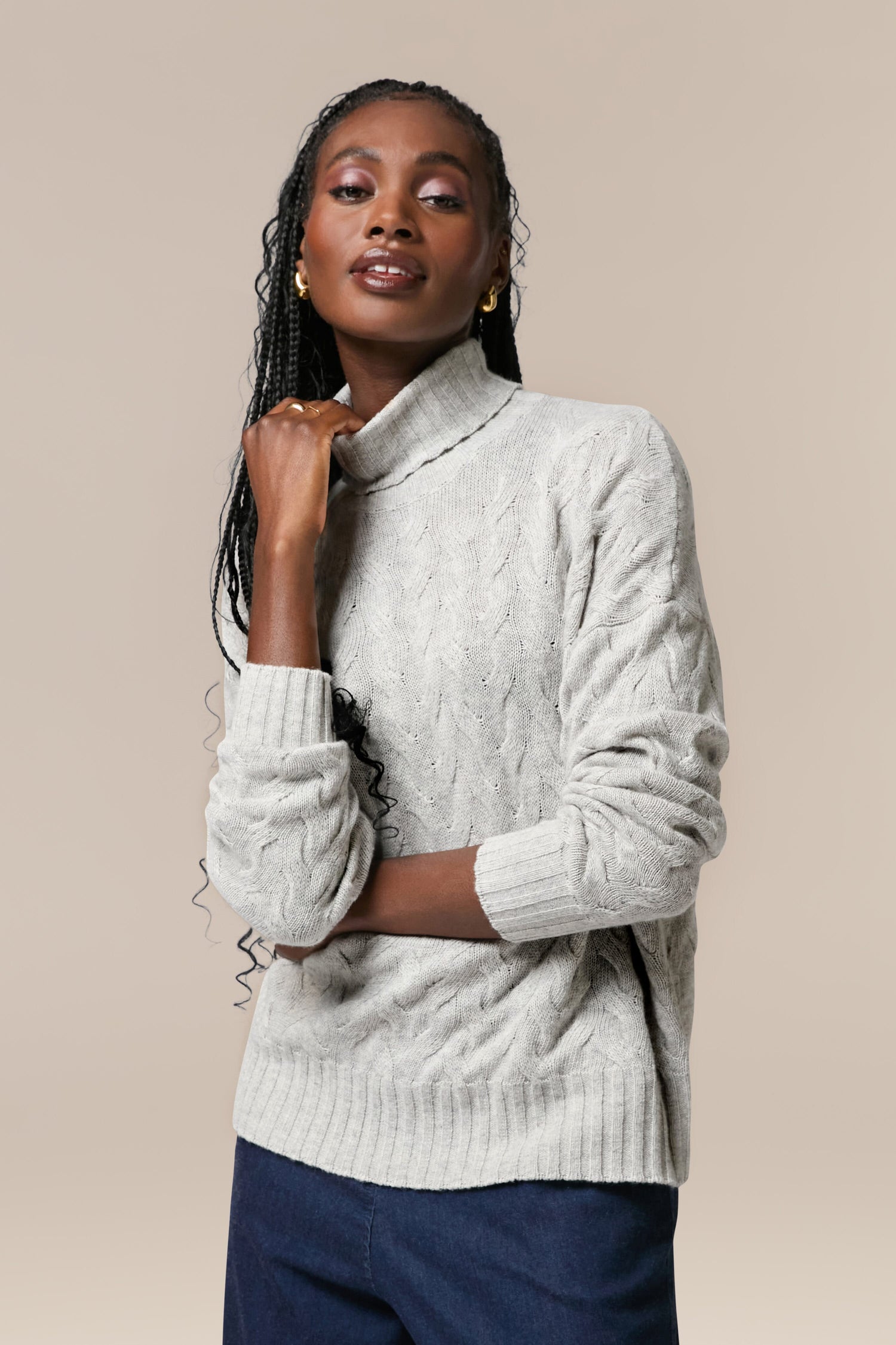 The model is wearing a grey quality Cable Knit Jumper made from merino wool and blue pants.