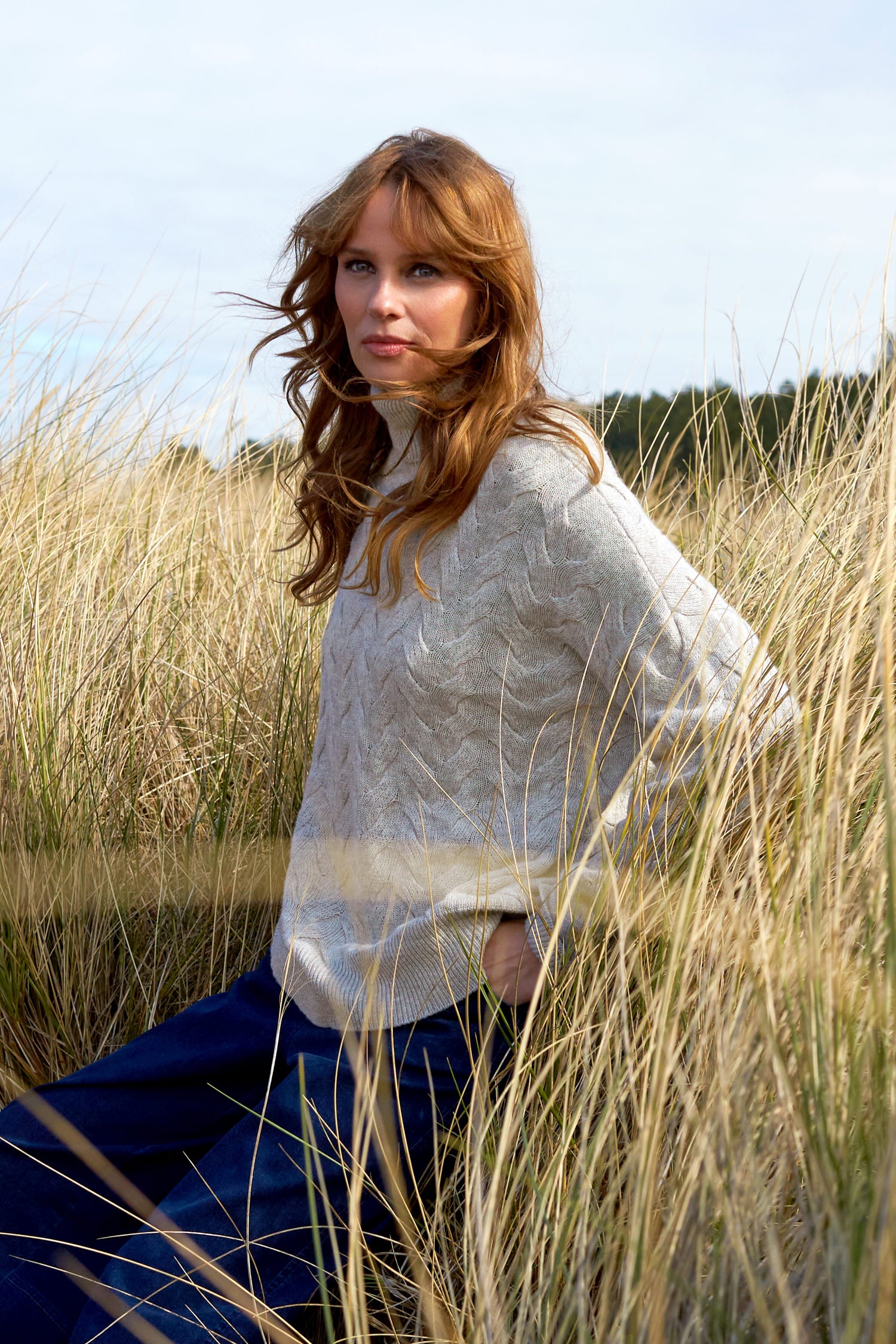A woman in a Cable Knit Jumper sitting in tall grass.