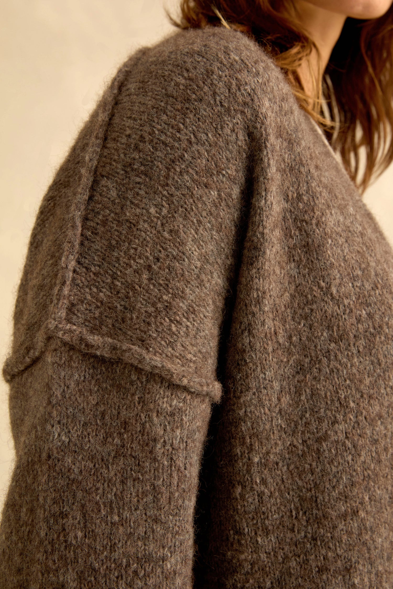 Close-up of a person wearing the Bark Alpaca Blend Long Line Cardigan, its textured brown wool blend and dropped shoulder seams framing their face and neck—an elegant showcase of women’s knitwear classics.
