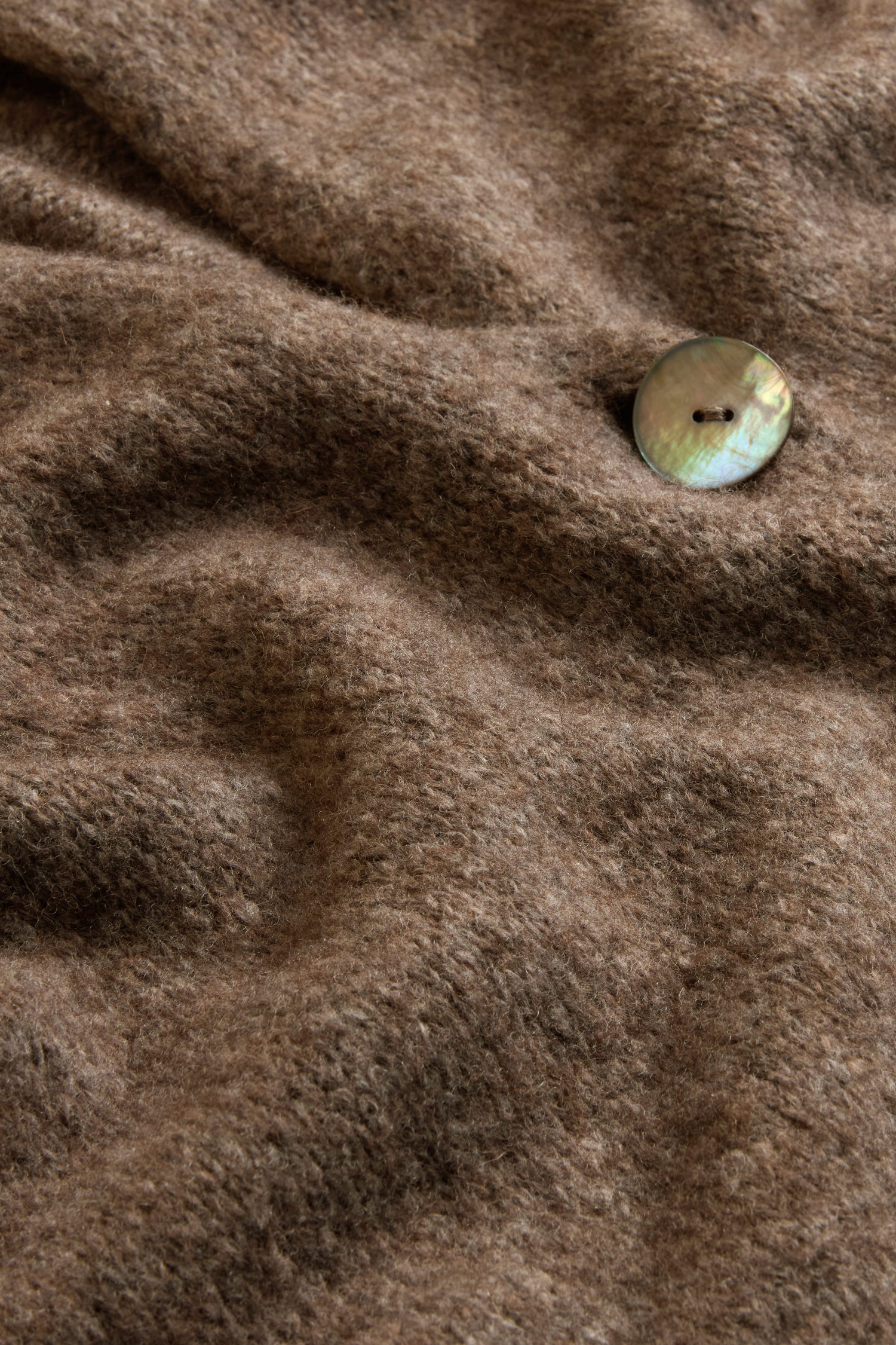 Close-up of a brown woolen fabric from the Bark Alpaca Blend Long Line Cardigan, featuring a single iridescent round button sewn near the upper right corner—a perfect detail from this women’s knitwear piece.
