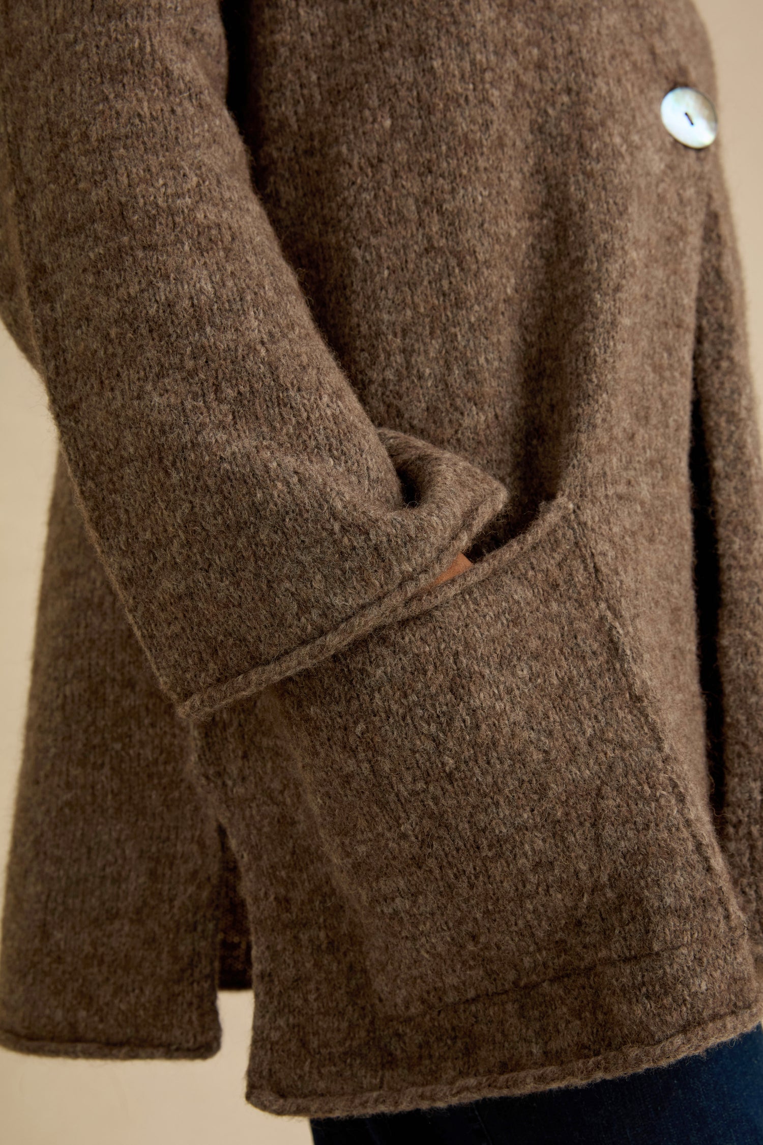 A person wearing the Bark Alpaca Blend Long Line Cardigan—textured brown wool, with one hand partially tucked into a spacious front pocket and a visible button near the top.