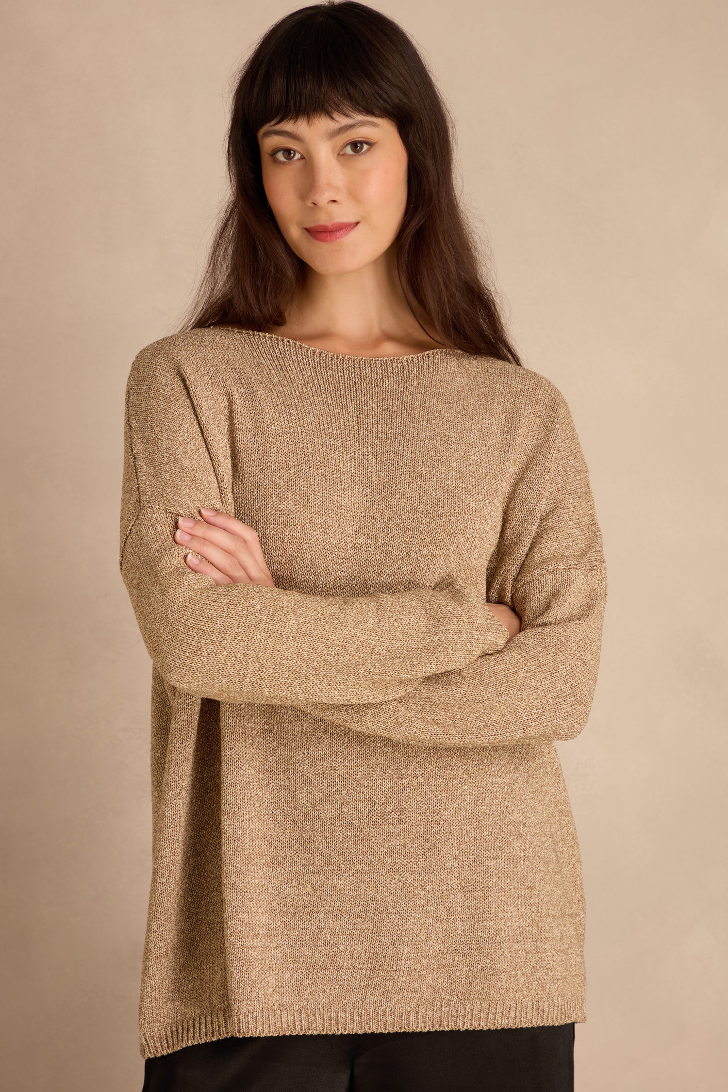 Woman with long dark hair and bangs wears the Champagne Boxy Sparkle Knit Jumper and black pants, standing arms crossed against a neutral background.