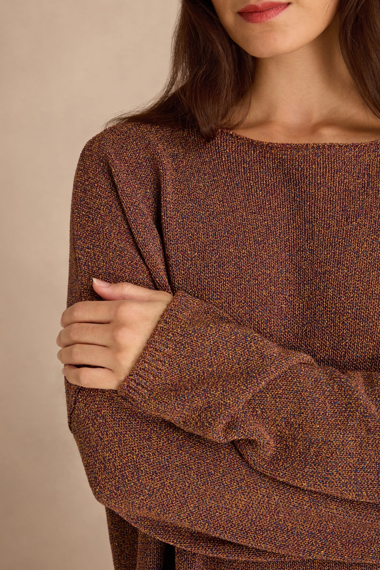 A woman with long brown hair wears the Copper Boxy Sparkle Knit Jumper, crossing her arms over her chest with her face partially visible.