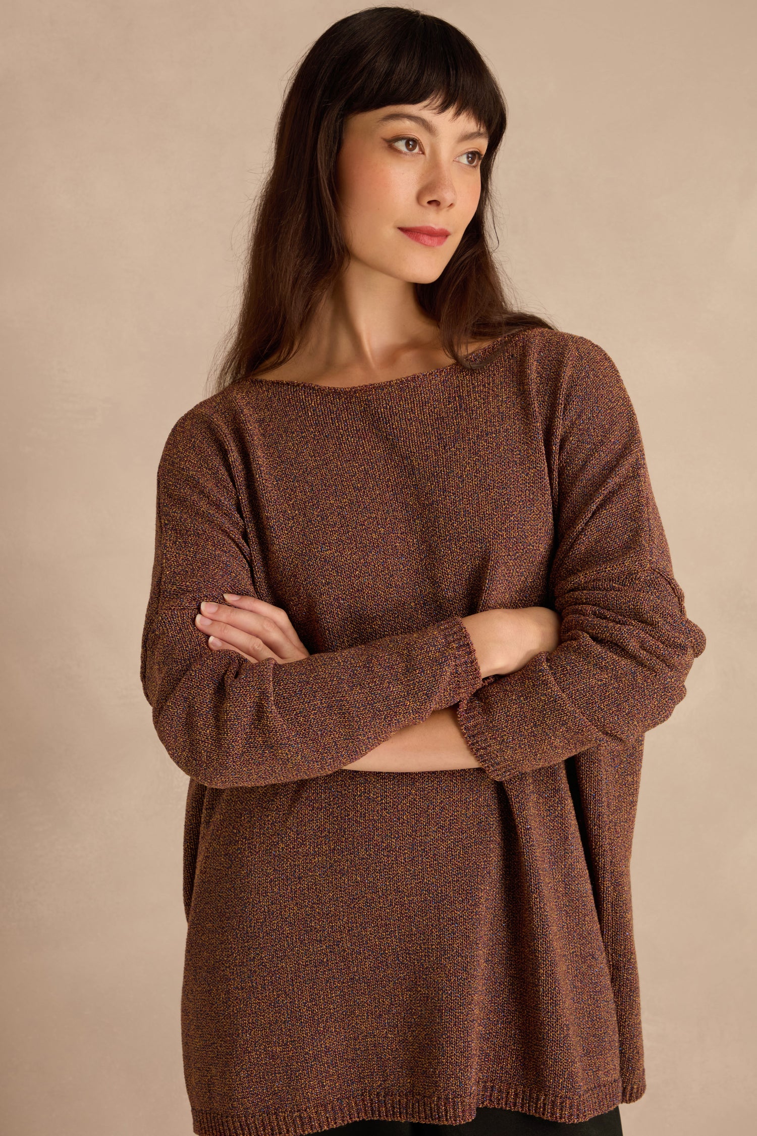 Woman with long dark hair and bangs wears the Copper Boxy Sparkle Knit Jumper, standing with arms crossed against a neutral background.