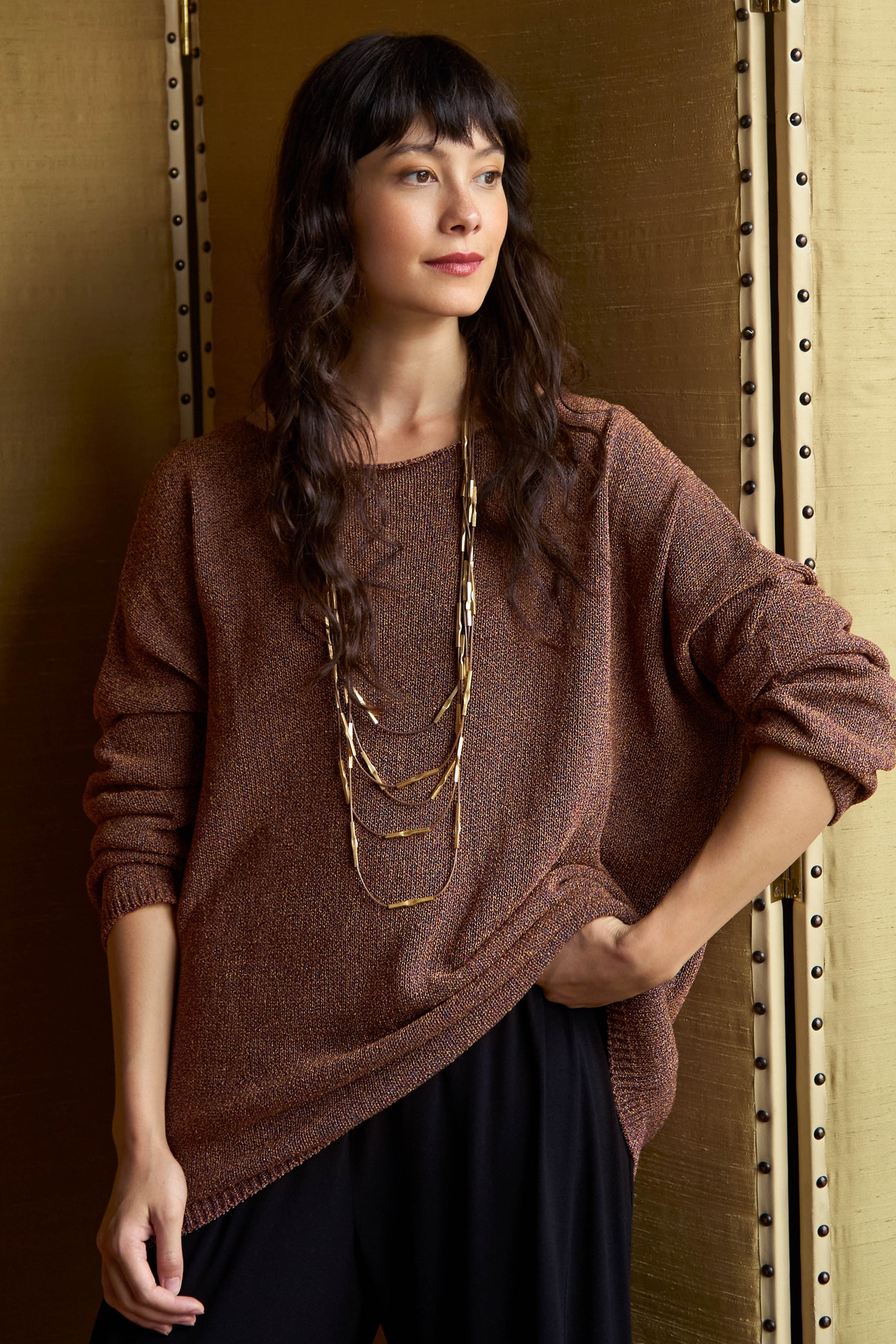 A person wearing a Copper Boxy Sparkle Knit Jumper in a metallic copper Italian knit with a boxy silhouette and a multi-strand gold necklace.