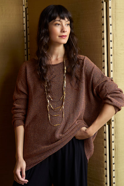 A person wearing a Copper Boxy Sparkle Knit Jumper in a metallic copper Italian knit with a boxy silhouette and a multi-strand gold necklace.