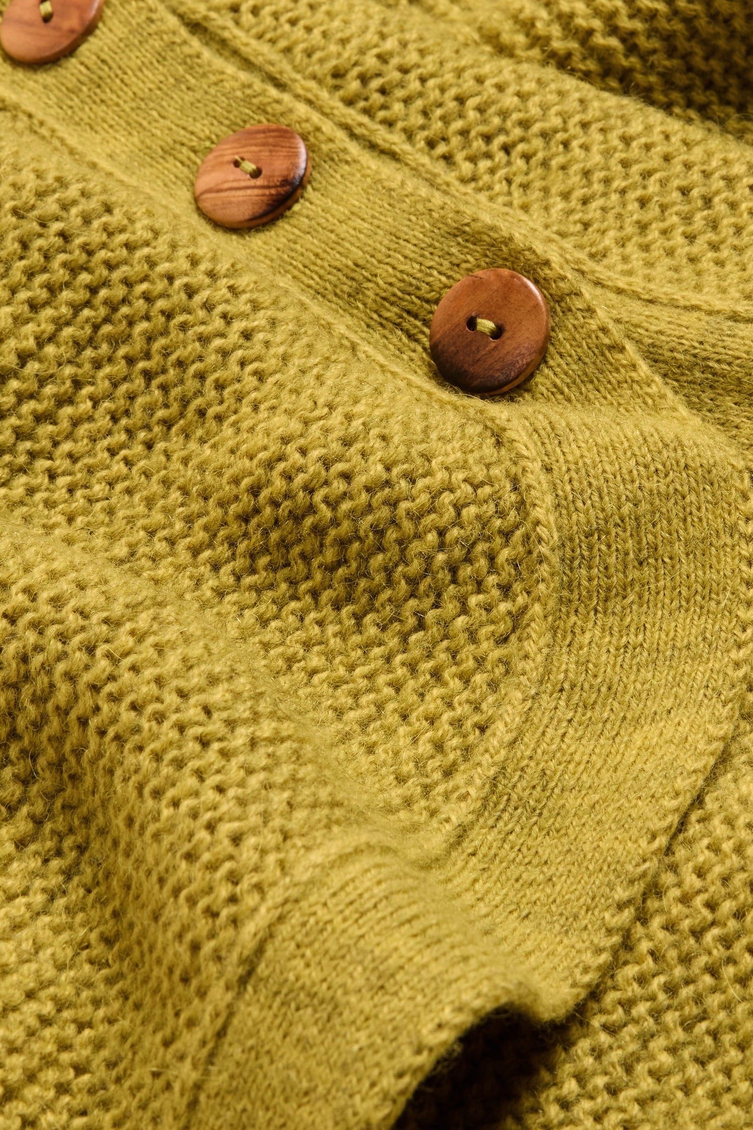 Close-up of the Avocado Ribbed Wool Blend Button Jumper, showcasing its textured yellow ribbed knit and three round wooden buttons sewn along a vertical edge—a charming side button detail reminiscent of classic sweater styles.