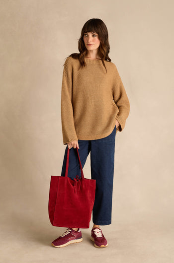 A woman wearing the Camel Ribbed Wool Blend Button Jumper, blue jeans, and red sneakers, holding a large red tote bag, stands against a neutral background.