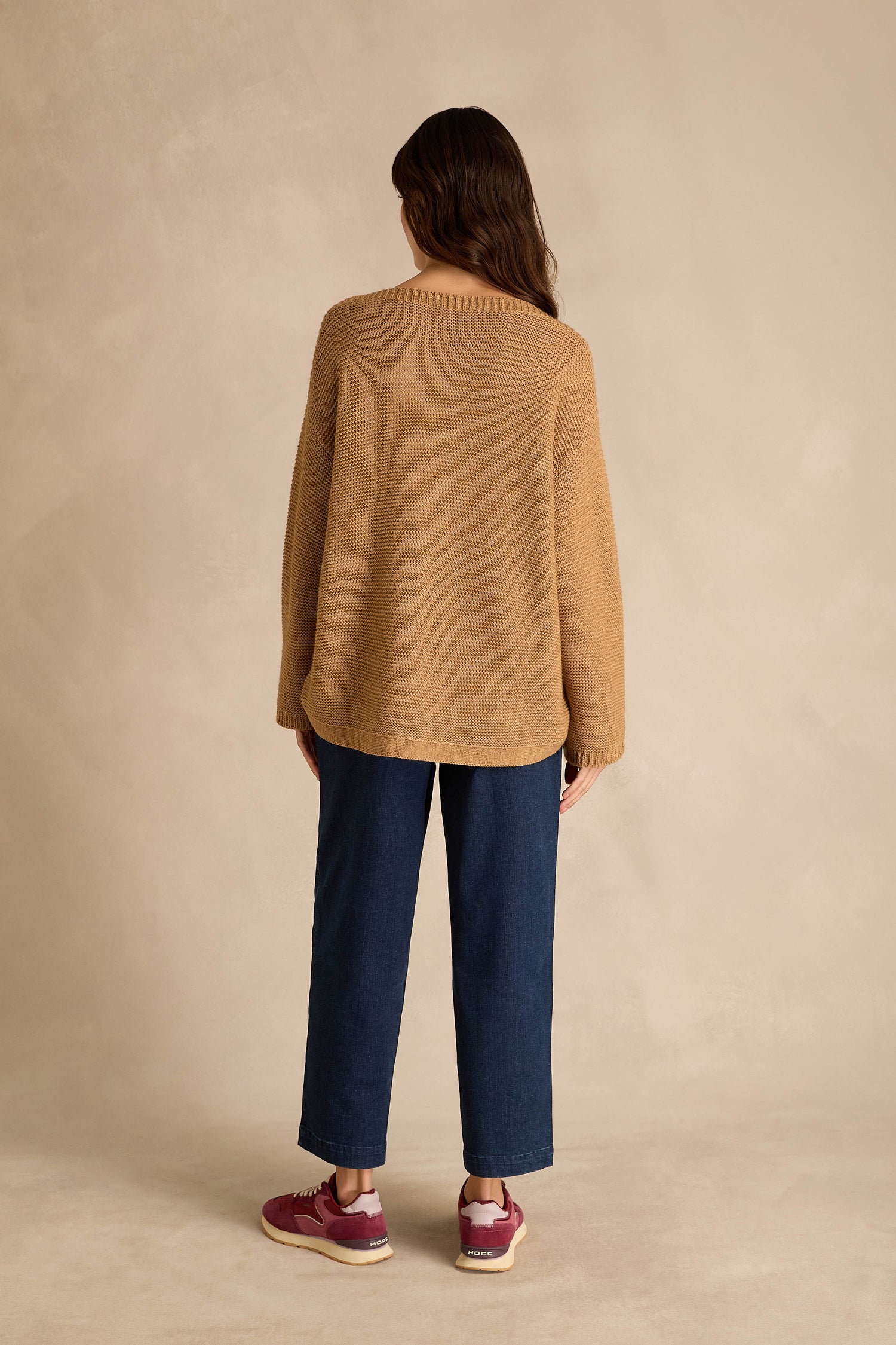 A person stands facing away against a plain beige background, wearing the Camel Ribbed Wool Blend Button Jumper, dark blue pants, and maroon sneakers.