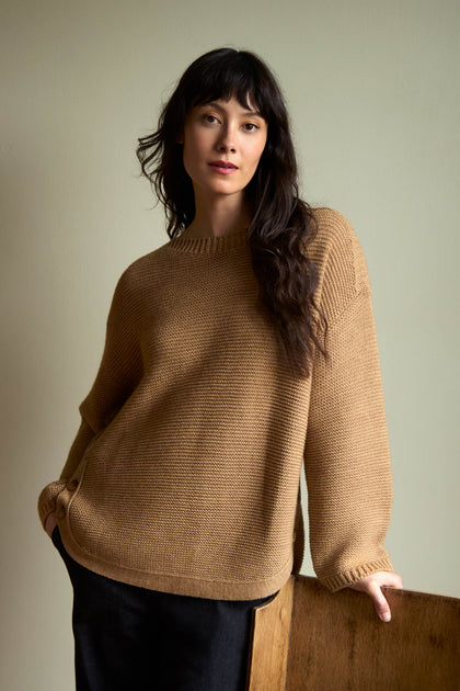 A person wears a camel-colored, ribbed wool Camel Ribbed Wool Blend Button Jumper with buttons at the hip.