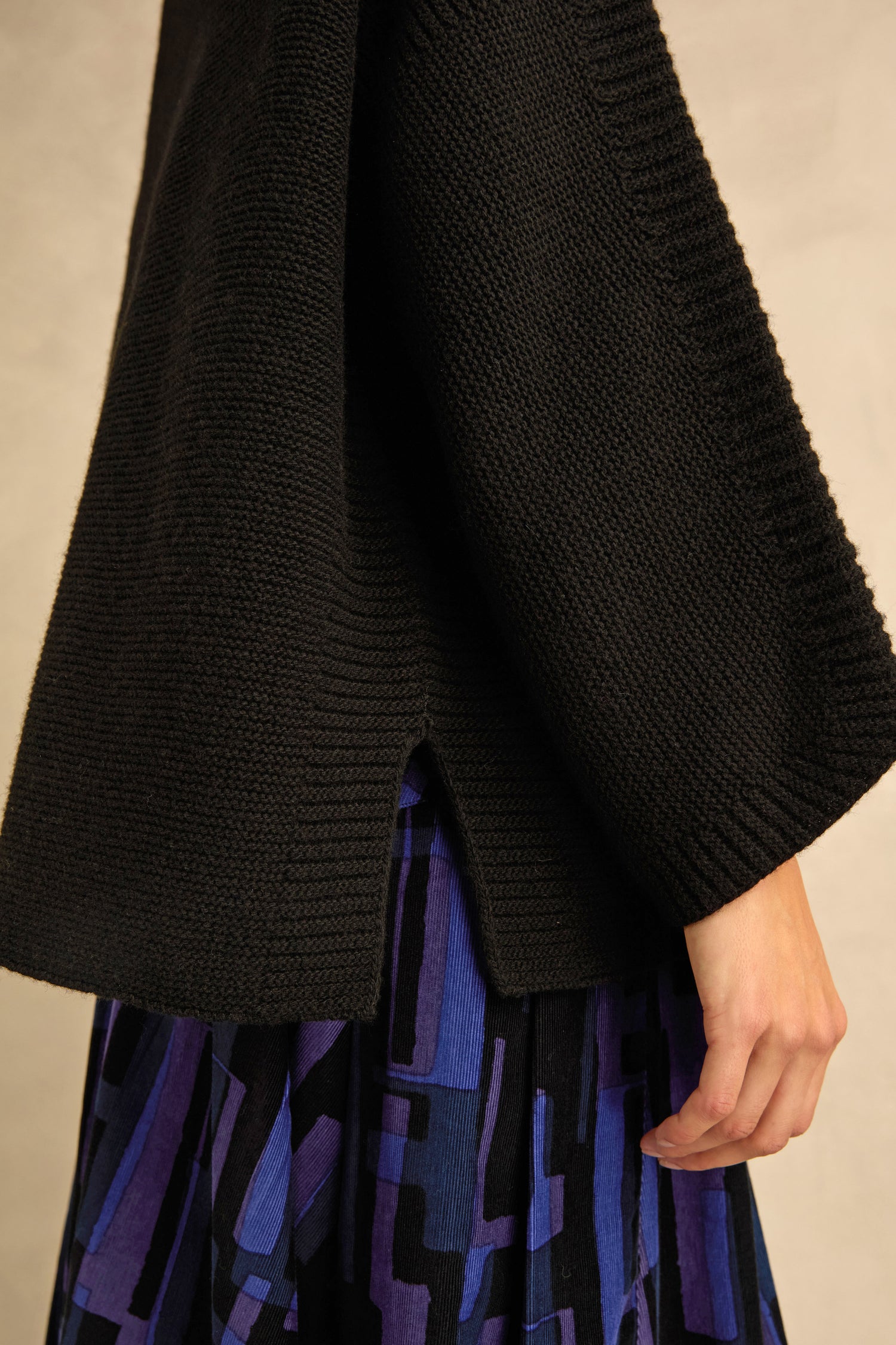 A person wearing a Black Merino Ribbed Turtle Neck Jumper and a blue and black patterned skirt, shown from the side.