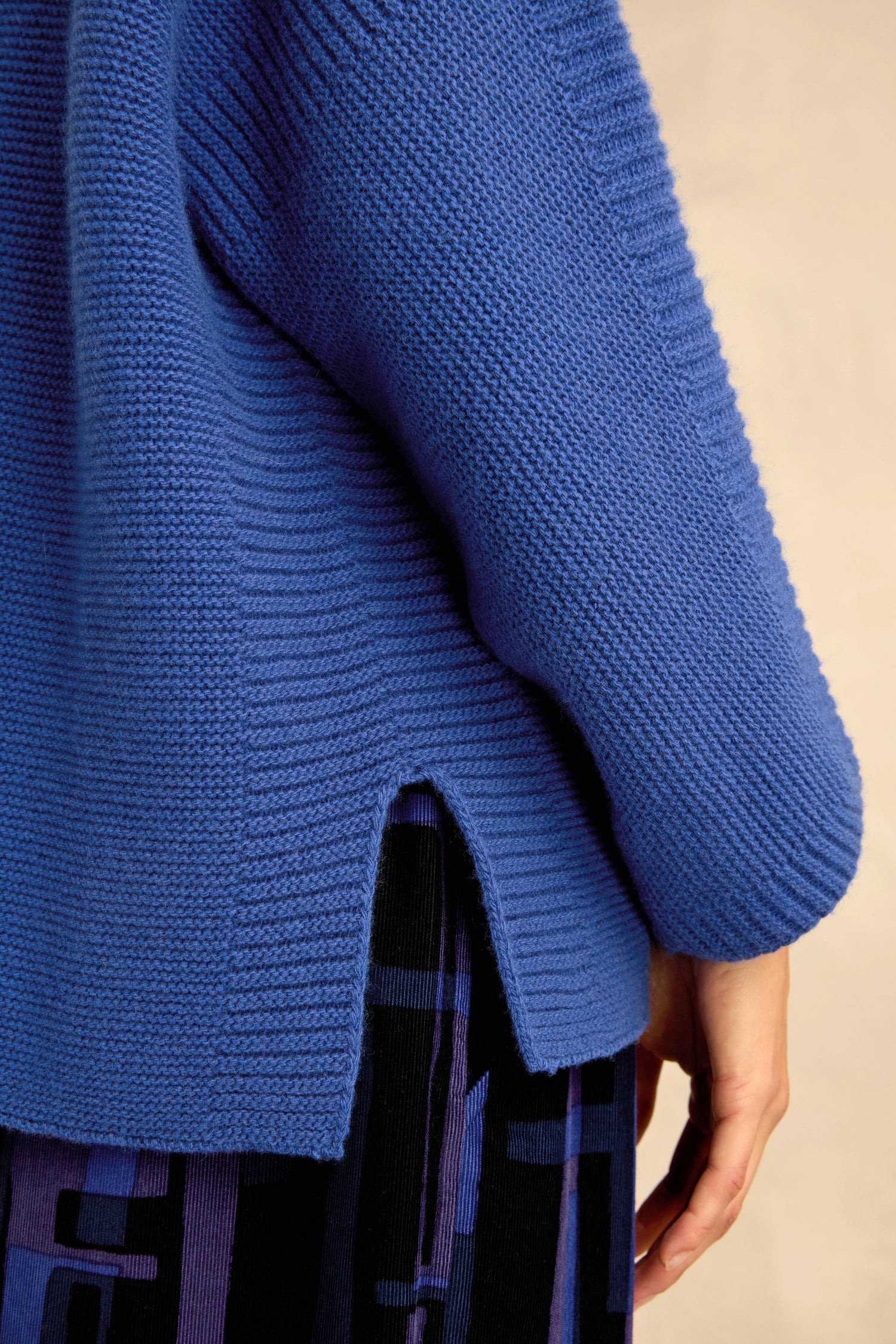 Close-up of a person wearing the Royal Blue Merino Ribbed Turtle Neck Jumper, styled with a dark skirt featuring a blue geometric pattern.