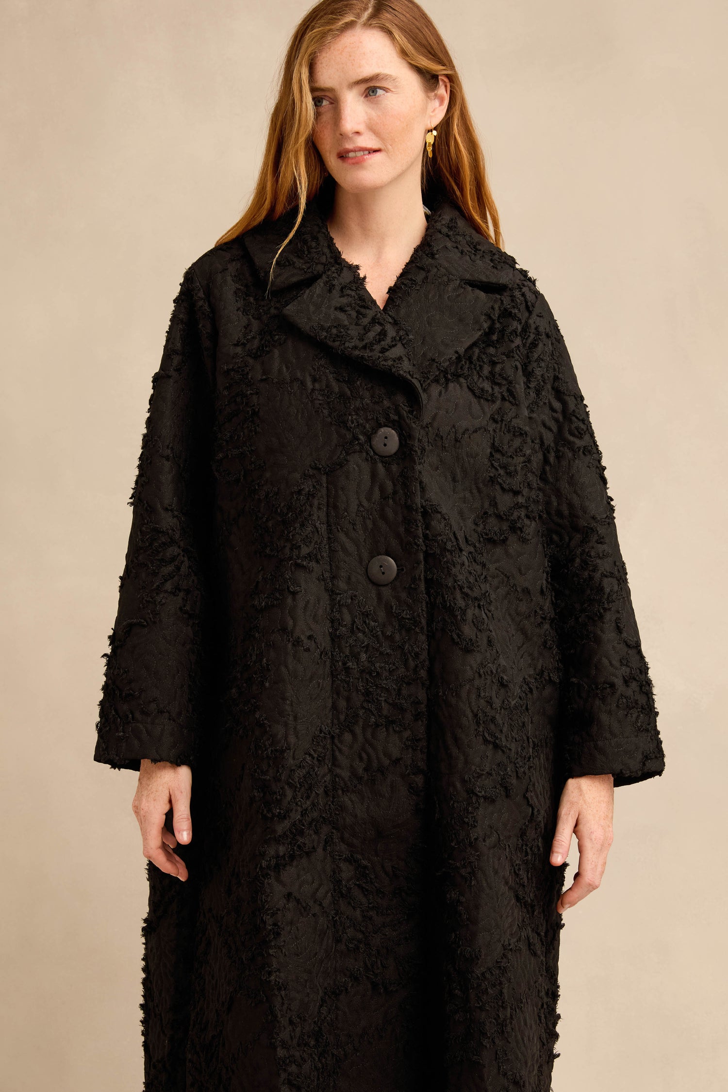A woman models the Textural Big Collar Coat, featuring large buttons, while standing against a plain beige background.