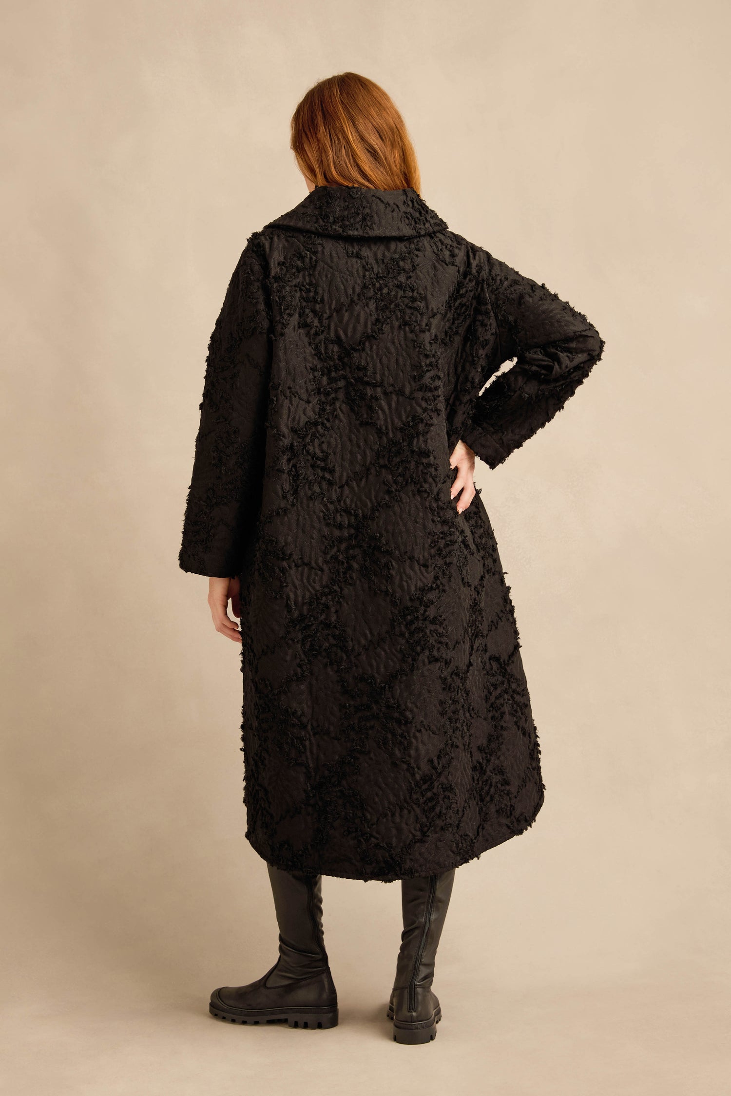 A person stands with their back turned, wearing the Textural Big Collar Coat in black paired with black boots, set against a neutral background.