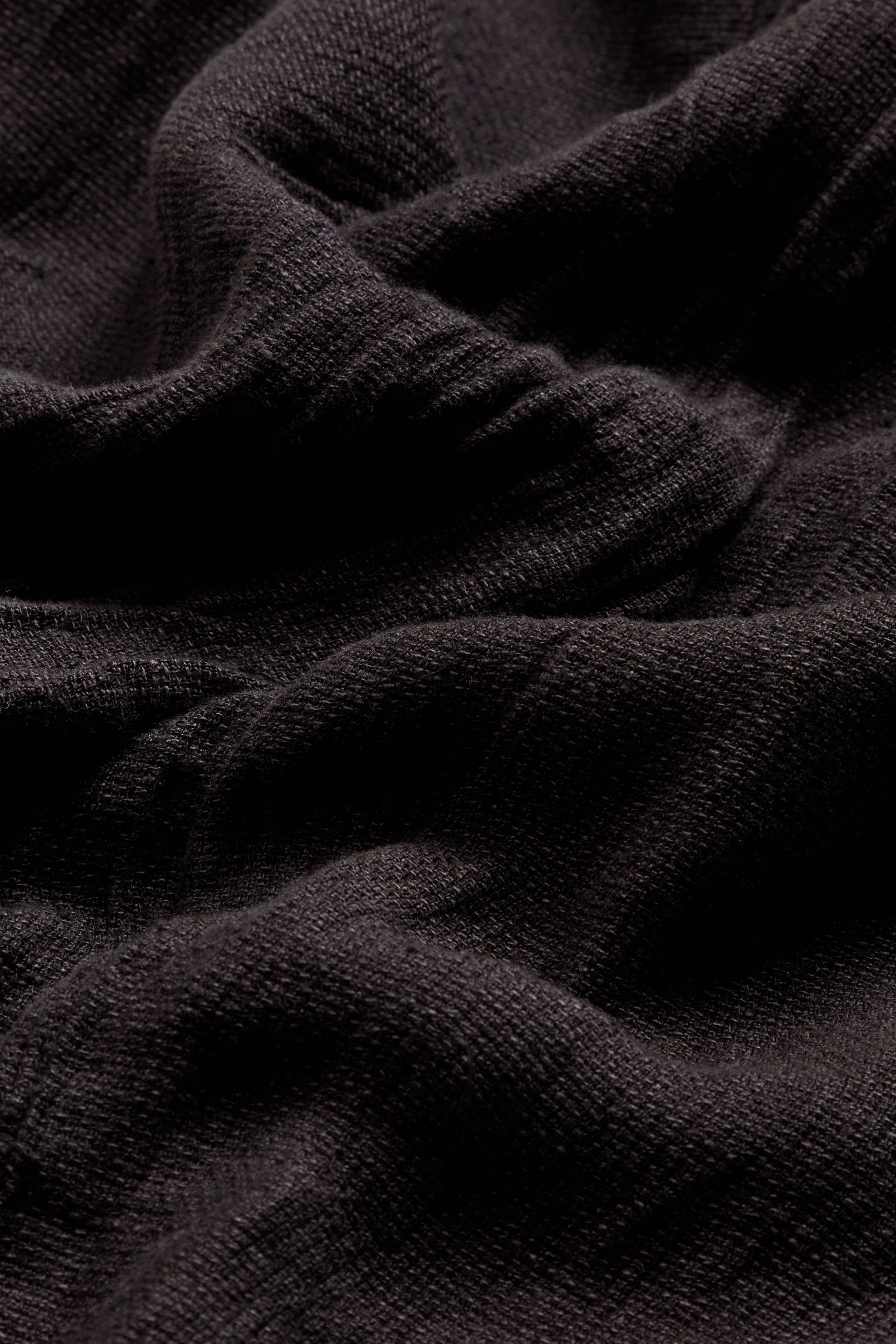 Close-up of the black, textured fabric of the Textured Linen Charcoal Bubble Trousers, featuring soft folds and visible fibers, recalling breathable natural materials—perfect for crafting bubble silhouette pants.