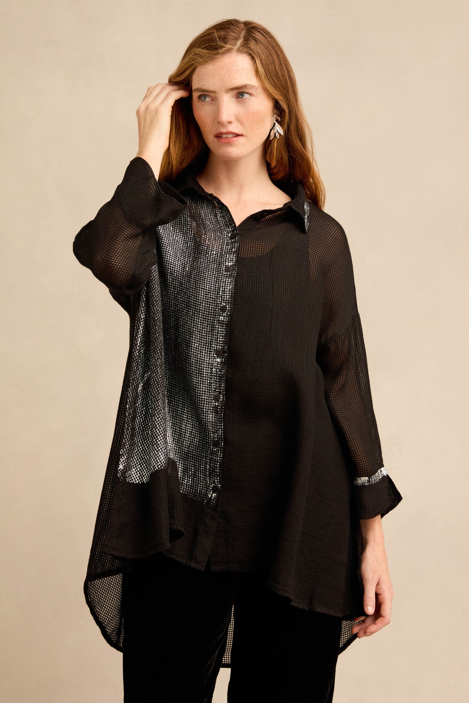 A woman wears the Sheer Silver Panel Flared Shirt—an airy, loose-fitting blouse with metallic silver panels and shiny accents—standing against a plain beige background.
