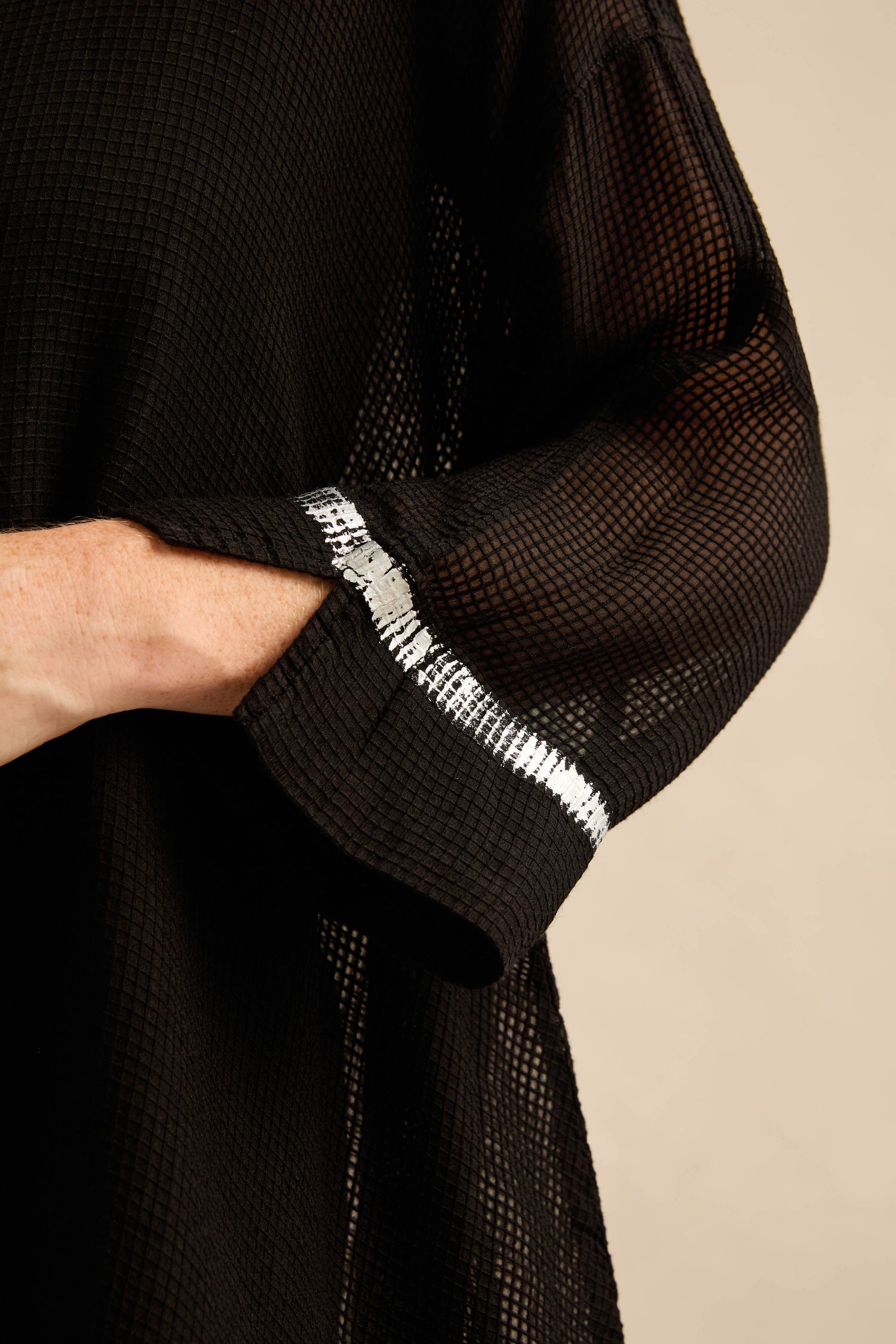 Close-up of a person’s arm wearing a black textured garment with a white stitched accent near the wrist, layered beneath the Sheer Silver Panel Flared Shirt for an elegant, modern contrast.