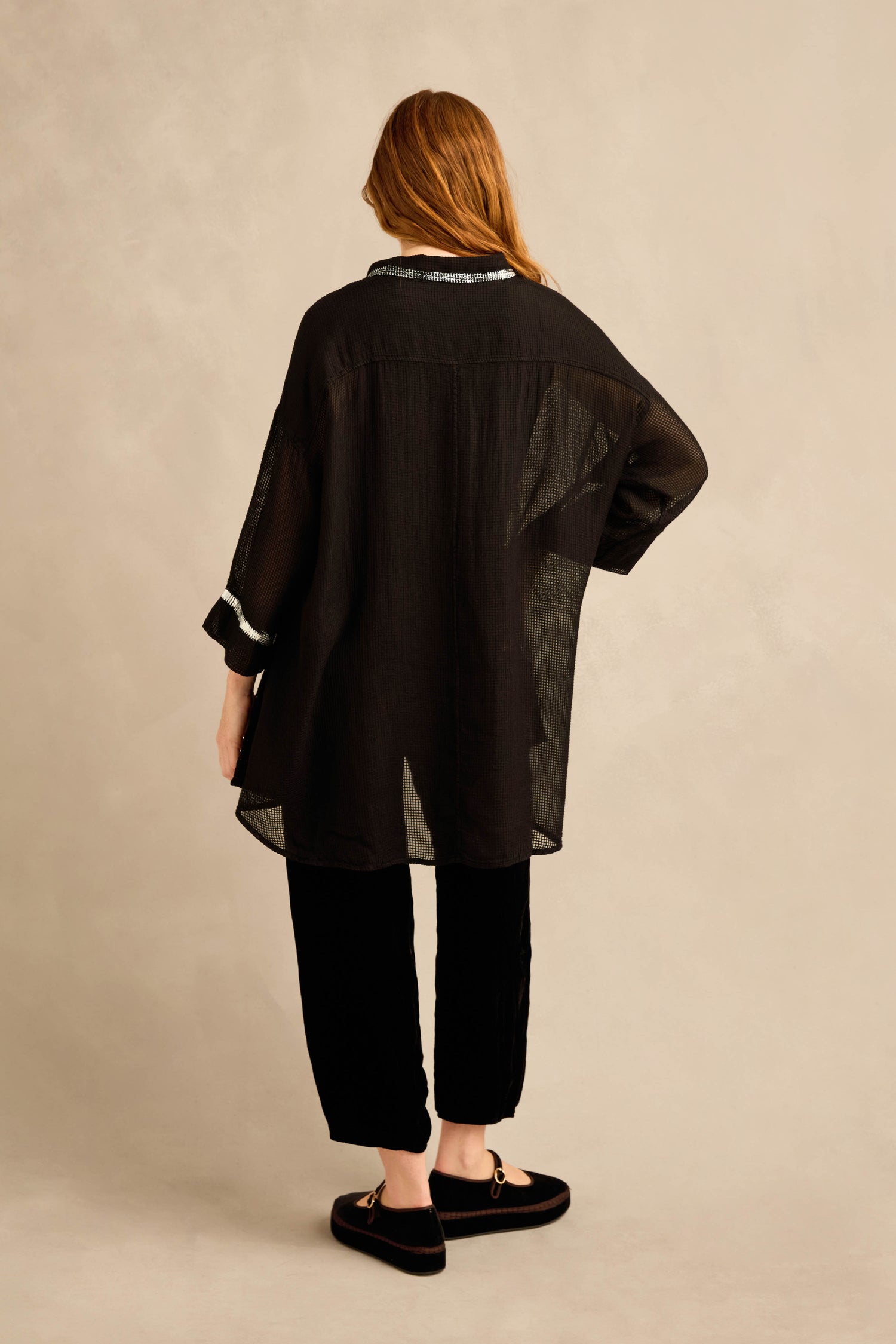 Person with long hair, wearing a Sheer Silver Panel Flared Shirt, black pants, and black loafers, standing with their back to the camera against a neutral background.
