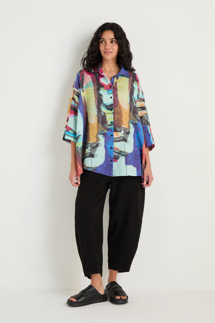 A person stands against a plain background wearing the Abstract Print Flared Shirt, paired with loose black pants and black sandals.