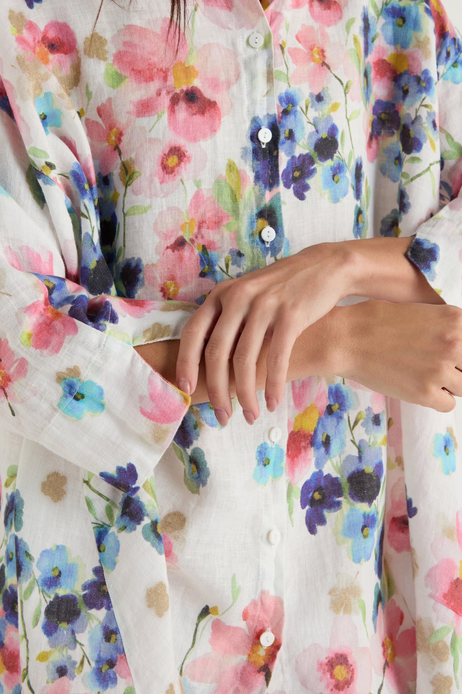 A person wearing the Primrose Print Flared Linen Shirt in a colorful floral design, shown in a close-up of their crossed arms and hands.