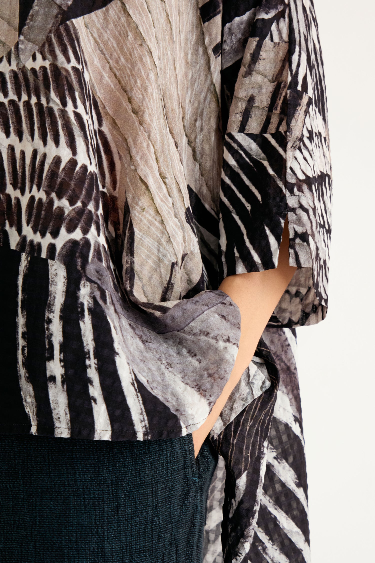A person wears the Patchwork Print Flared Shirt in black and beige print, with one hand tucked into the pocket of dark textured pants.