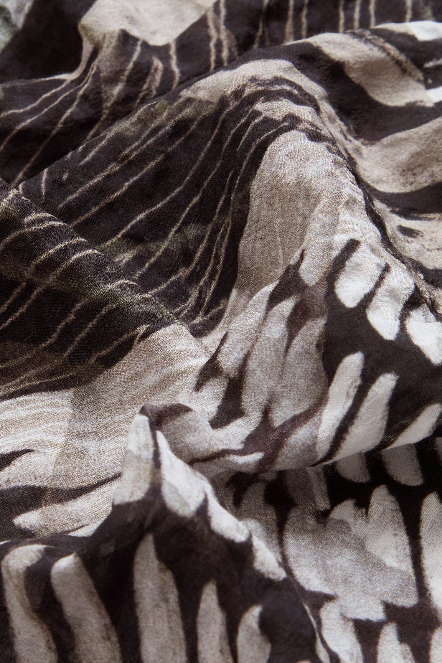 Close-up of crumpled fabric featuring a black and white abstract pattern evocative of tree branches or animal stripes, reminiscent of the distinctive designs on the Patchwork Print Flared Shirt.
