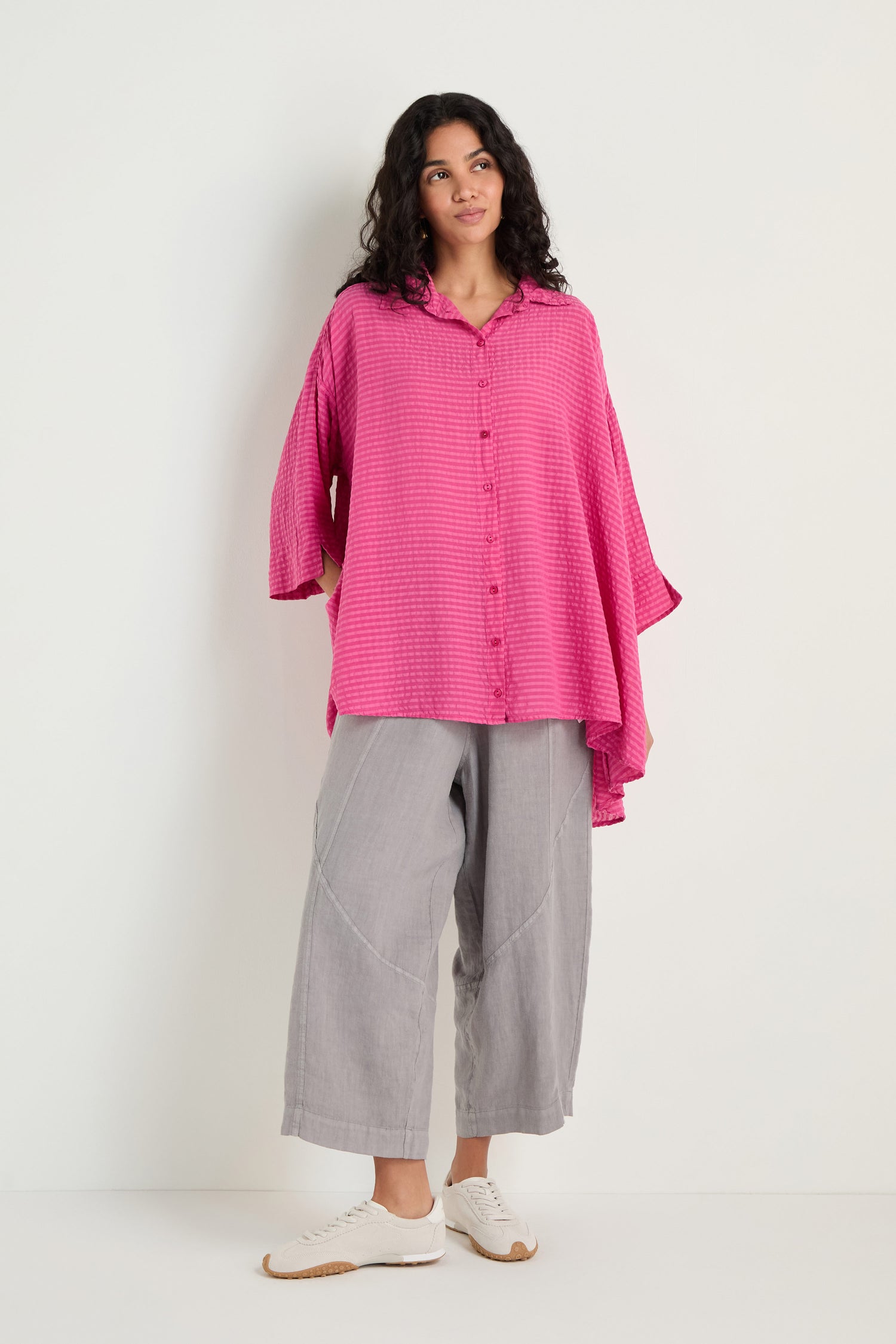 A person models the Seersucker Silk Blend Flared Shirt in fuchsia and wide-legged gray pants, standing against a plain white background.