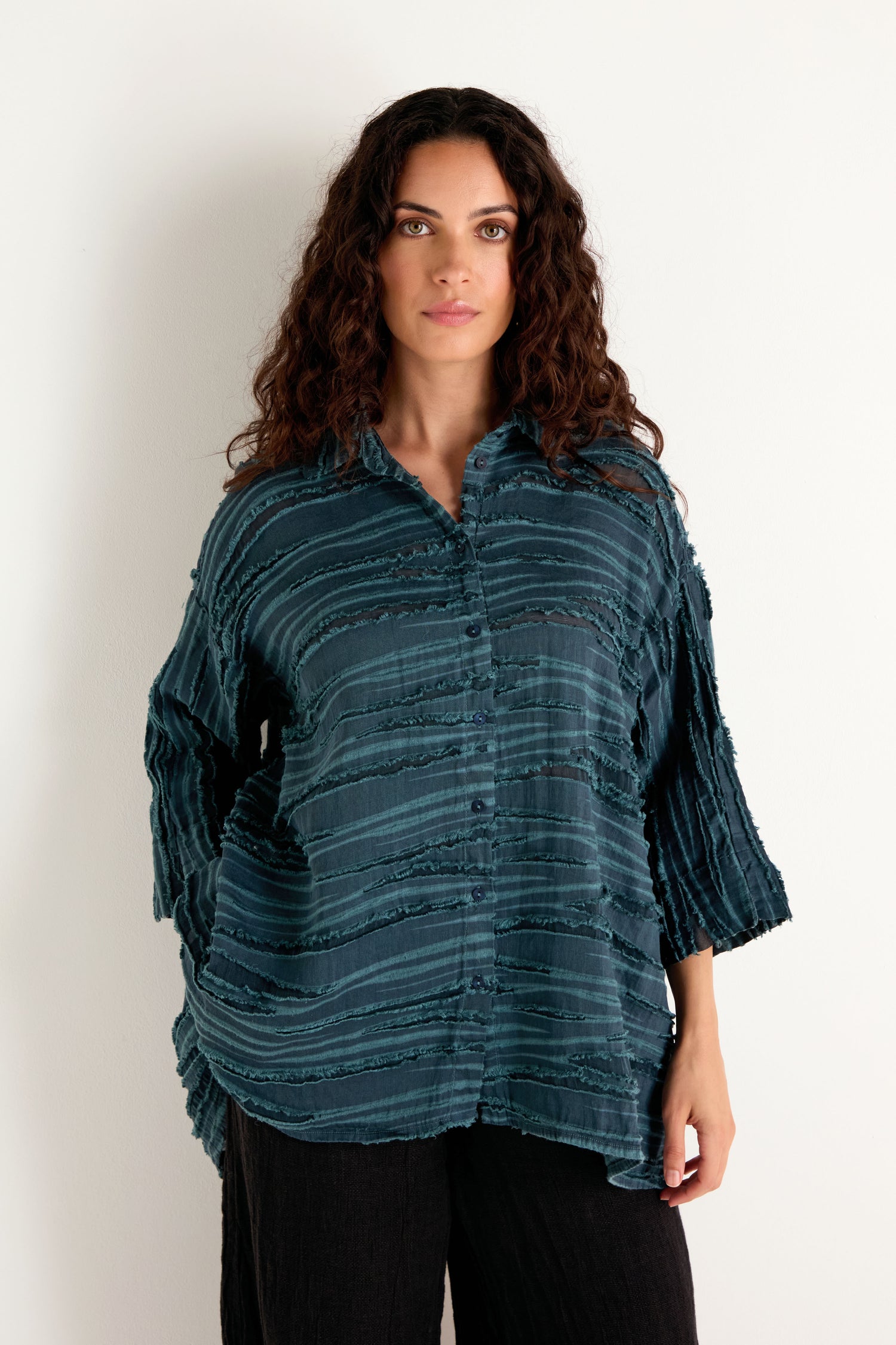 A woman with long curly hair wearing the Deep Turquoise Textured Stripe Flared Shirt and black pants, standing against a plain white background.
