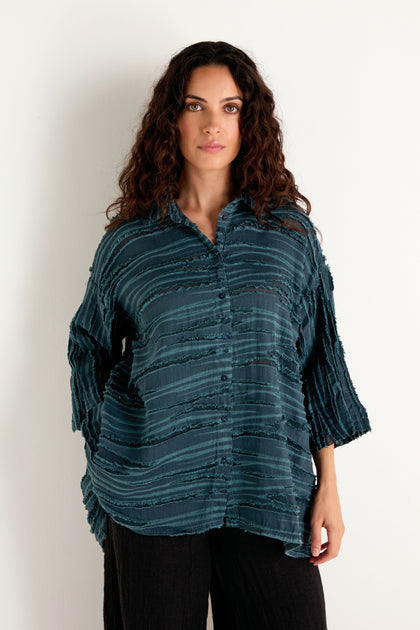 A woman with long curly hair wearing the Deep Turquoise Textured Stripe Flared Shirt and black pants, standing against a plain white background.