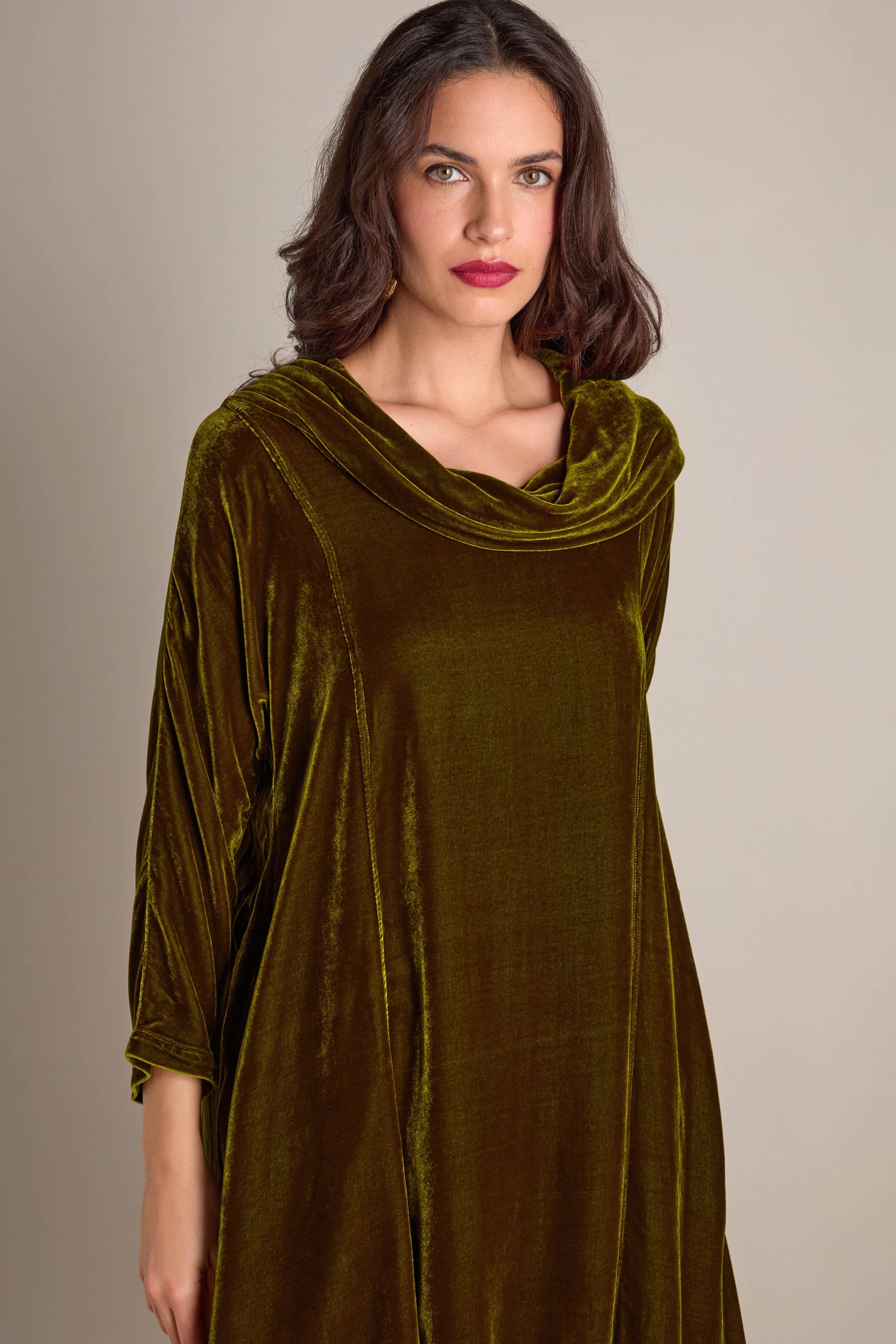 An individual is dressed in the Cowl Silk Velvet Dress, featuring a green hue, and stands against a neutral background.