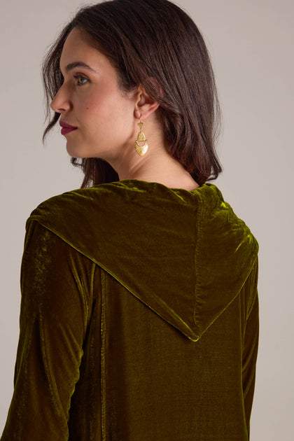 A woman with long dark hair in a Cowl Silk Velvet Dress and gold earrings, viewed from a side angle.