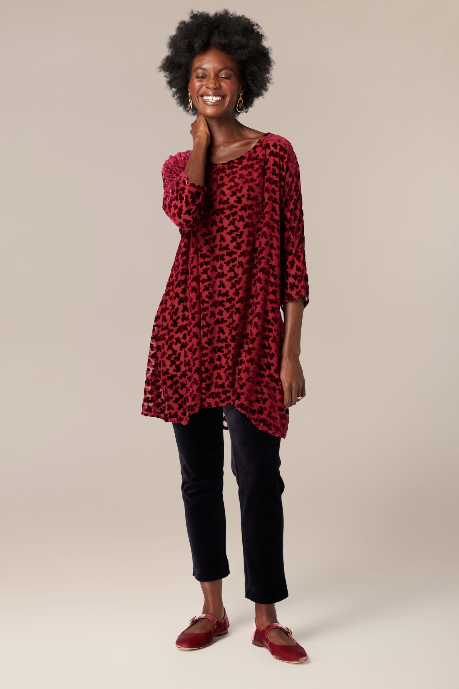 A woman wearing a Devore Tunic in a striking shade of red with black pants.