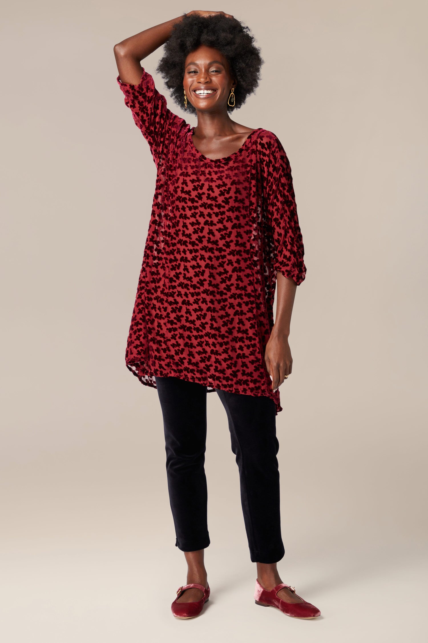 A Grizas Devore Tunic, worn gracefully by a black woman dressed in an elegant red Devore Tunic and black pants.