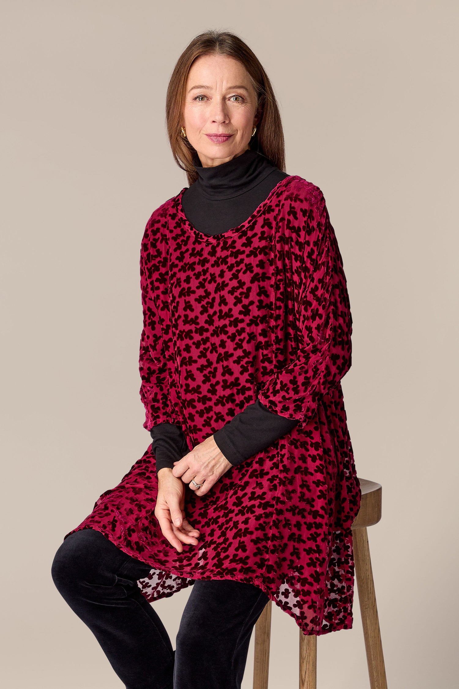 A woman is sitting on a stool in a Devore Tunic made of burned-out velvet textile.