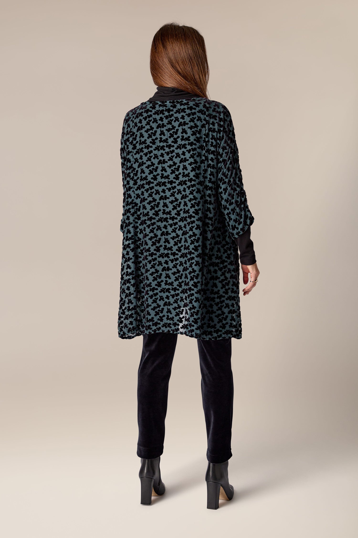 The woman is seen from behind, dressed in a Devore Tunic, a black leopard print jacket made of burned-out velvet textile.