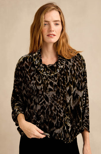 A woman with long red hair stands against a beige background wearing the Animal Print Cowl Neck Velvet Top, a loose-fitting black and brown velvet piece.