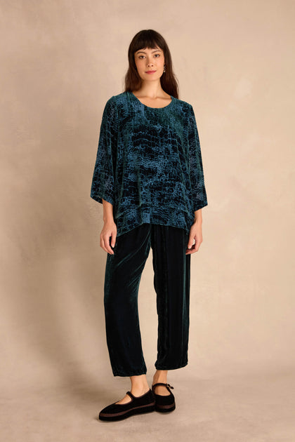 A person stands against a beige background wearing the Deep Turquoise Leopard Devore Layered top, matching relaxed pants, and black flat shoes.
