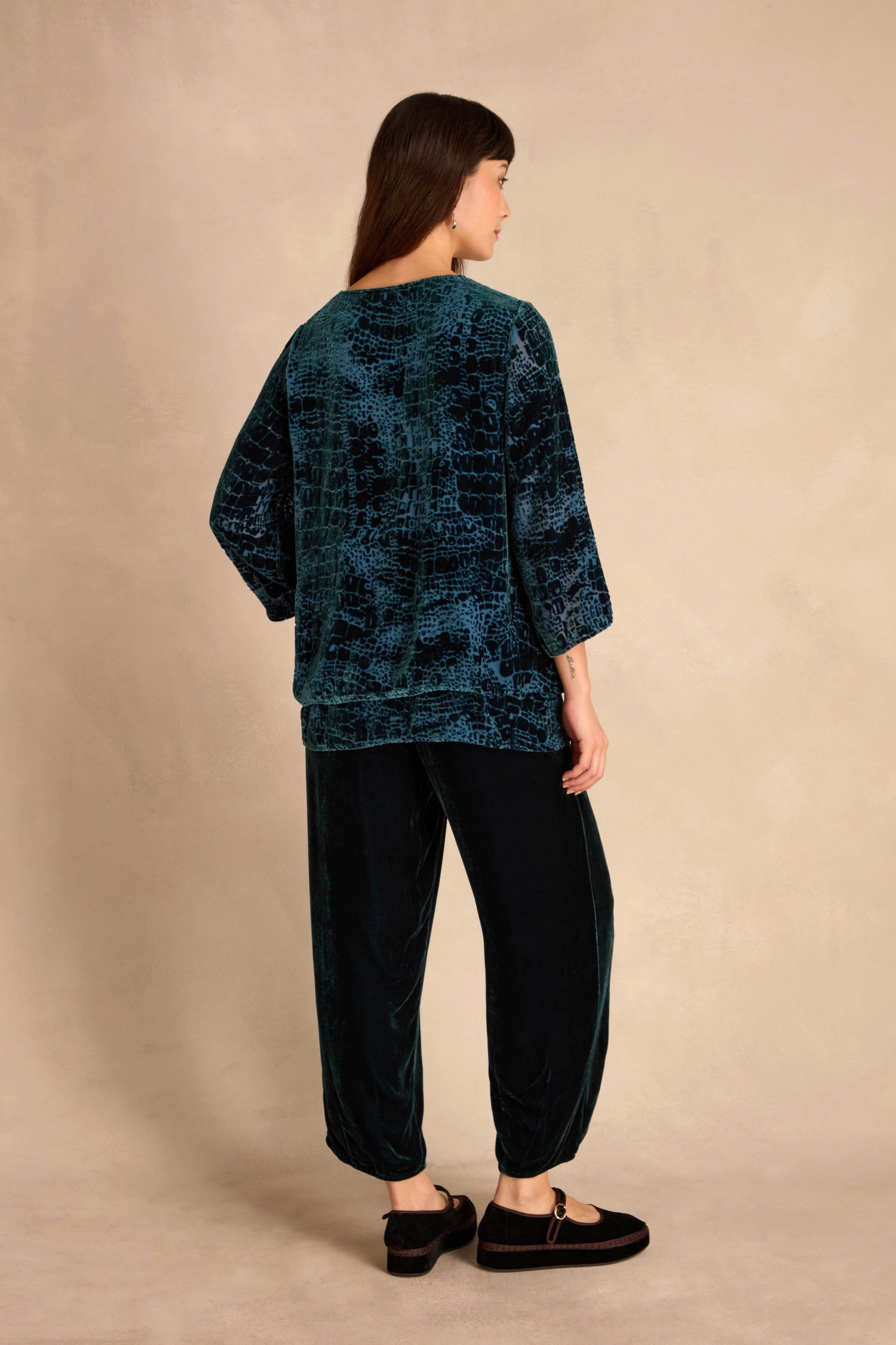 Woman stands against a beige background, wearing the Deep Turquoise Leopard Devore Layered top and matching pants with black flat shoes, facing slightly away from the camera.