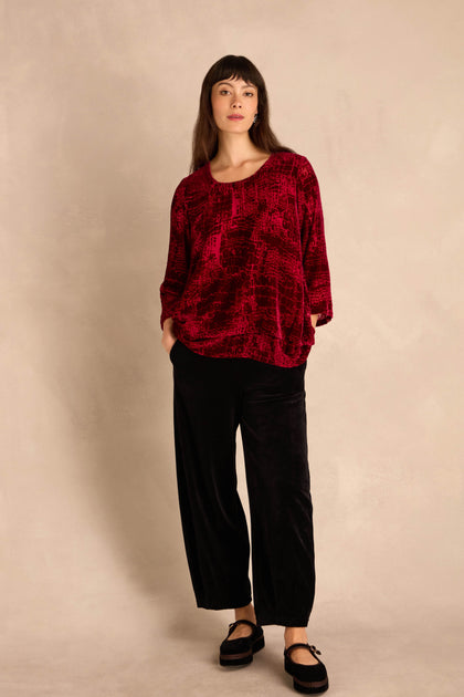 Woman stands against a light background wearing a loose Ruby Leopard Devore Layered Top, black wide-leg pants, and black shoes.