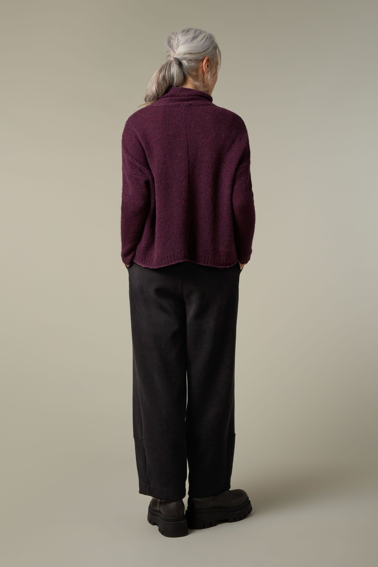 The back view of a woman wearing a plush knit Panel Knit sweater in a cozy layering outfit, paired with black pants.