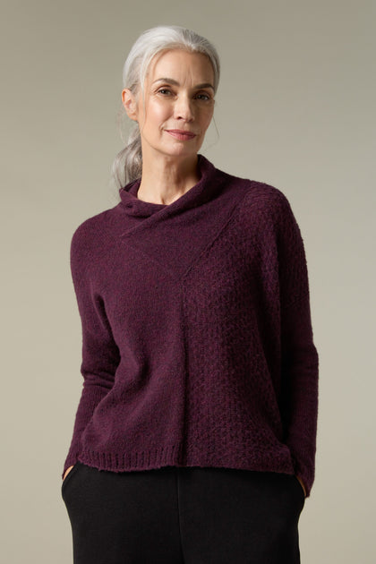 A woman wearing a Panel Knit burgundy plush knit sweater paired with black pants, providing a cosy layering option.