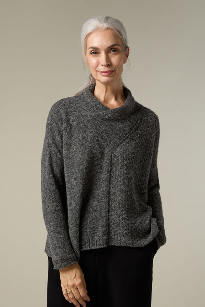 A woman wearing a plush Panel Knit grey sweater and cosy layering with black pants.