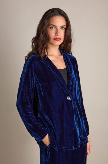 The woman exudes effortless chic in her Boxy Silk Velvet Jacket by Grizas, featuring its perfect layering design, with her hands tucked into the pockets against a neutral backdrop.