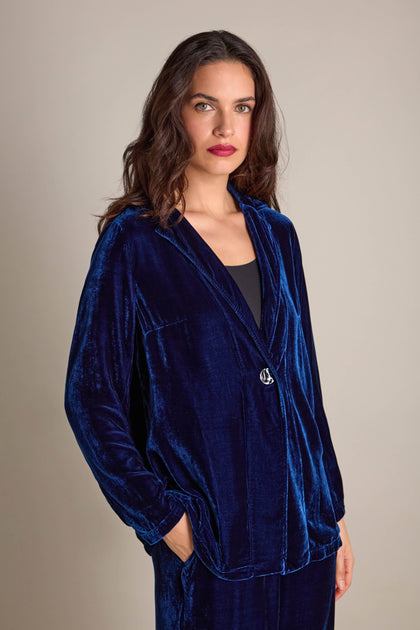 The woman exudes effortless chic in her Boxy Silk Velvet Jacket by Grizas, featuring its perfect layering design, with her hands tucked into the pockets against a neutral backdrop.