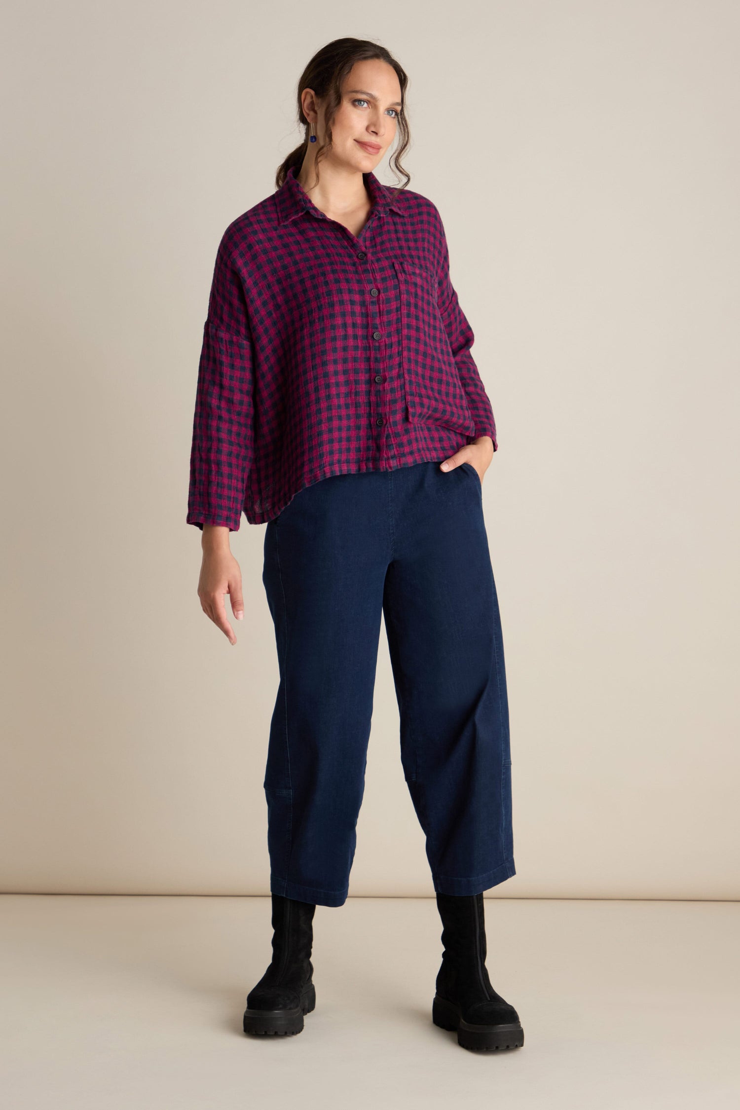 A person stands against a plain background wearing the Linen Check Big Pocket Shirt in red and blue, complemented by blue pants and black boots.