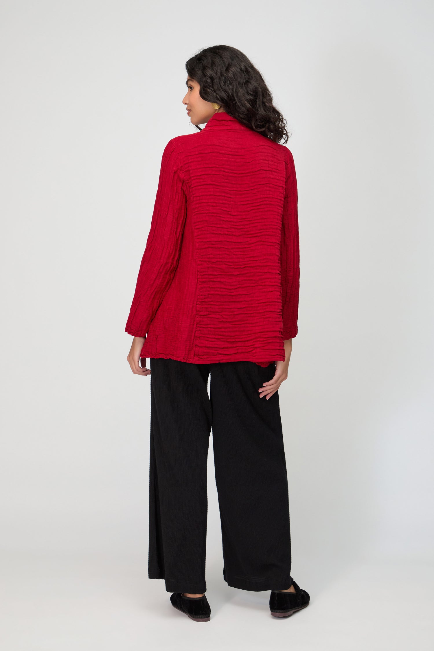 Woman standing with her back to the camera, wearing a textured red Panel Front Silk Linen Jacket, wide-leg black pants, and black shoes against a plain light background.