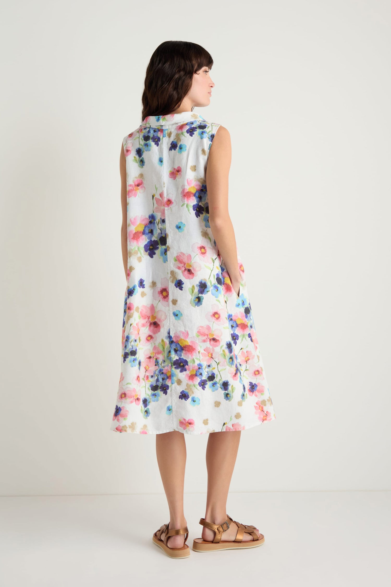 A woman faces away, wearing the Primrose Print Sleeveless Linen Dress with brown sandals.