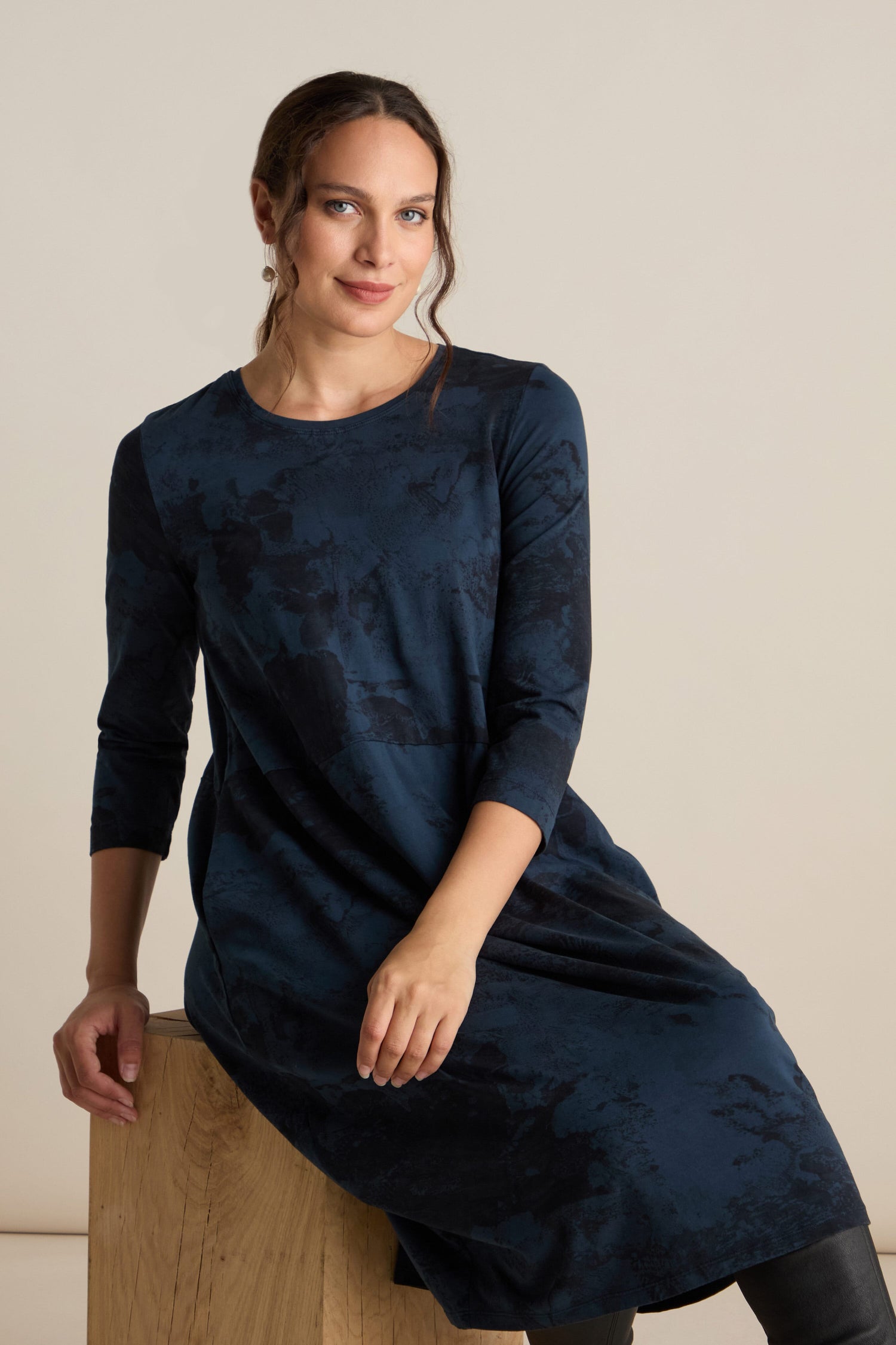 Person with brown hair wearing a dark blue, long-sleeve Print Bubble Jersey Dress sits on a wooden block against a plain background.